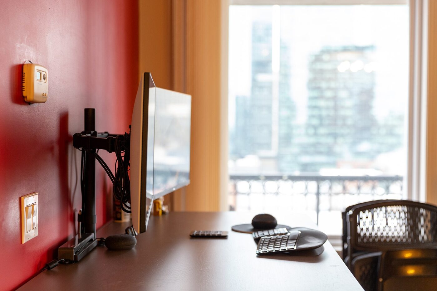 A flat-panel monitor mounted on a black articulating arm attached beside a desk, with the arm's pivot joint and mounting pole visible.