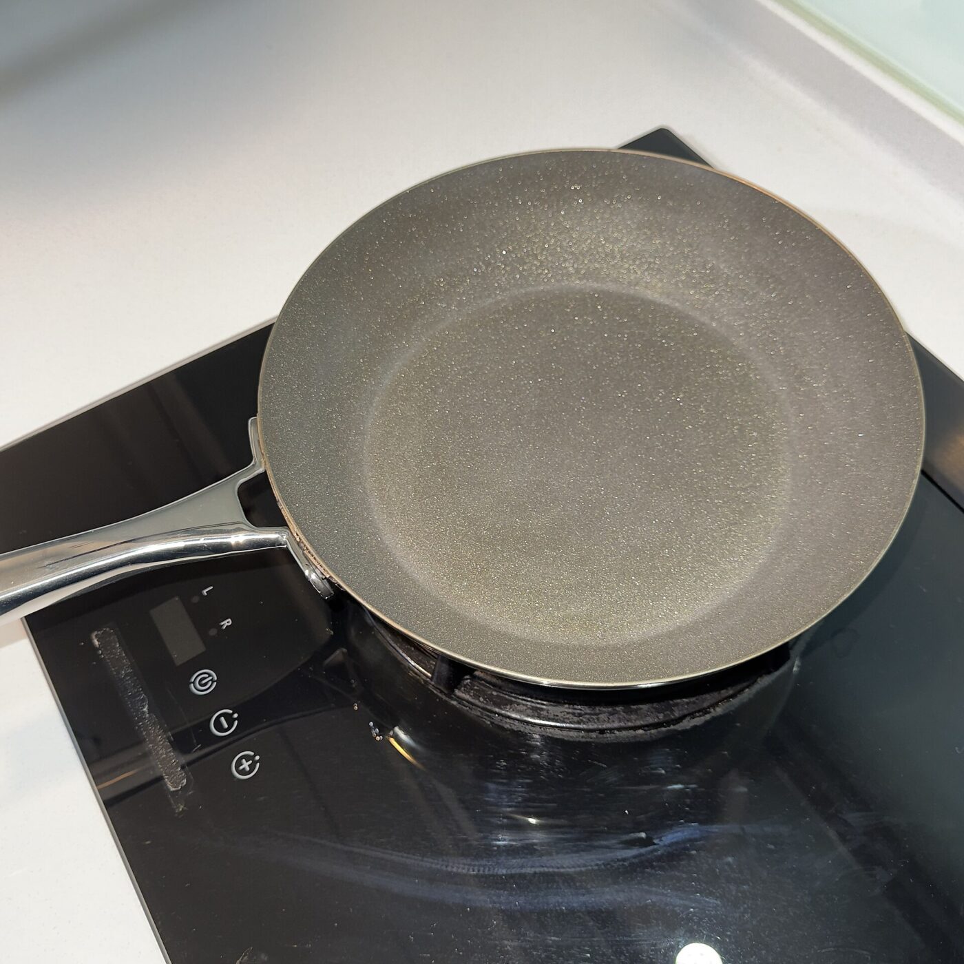 A dark nonstick frying pan with a speckled coating resting on a kitchen stovetop.