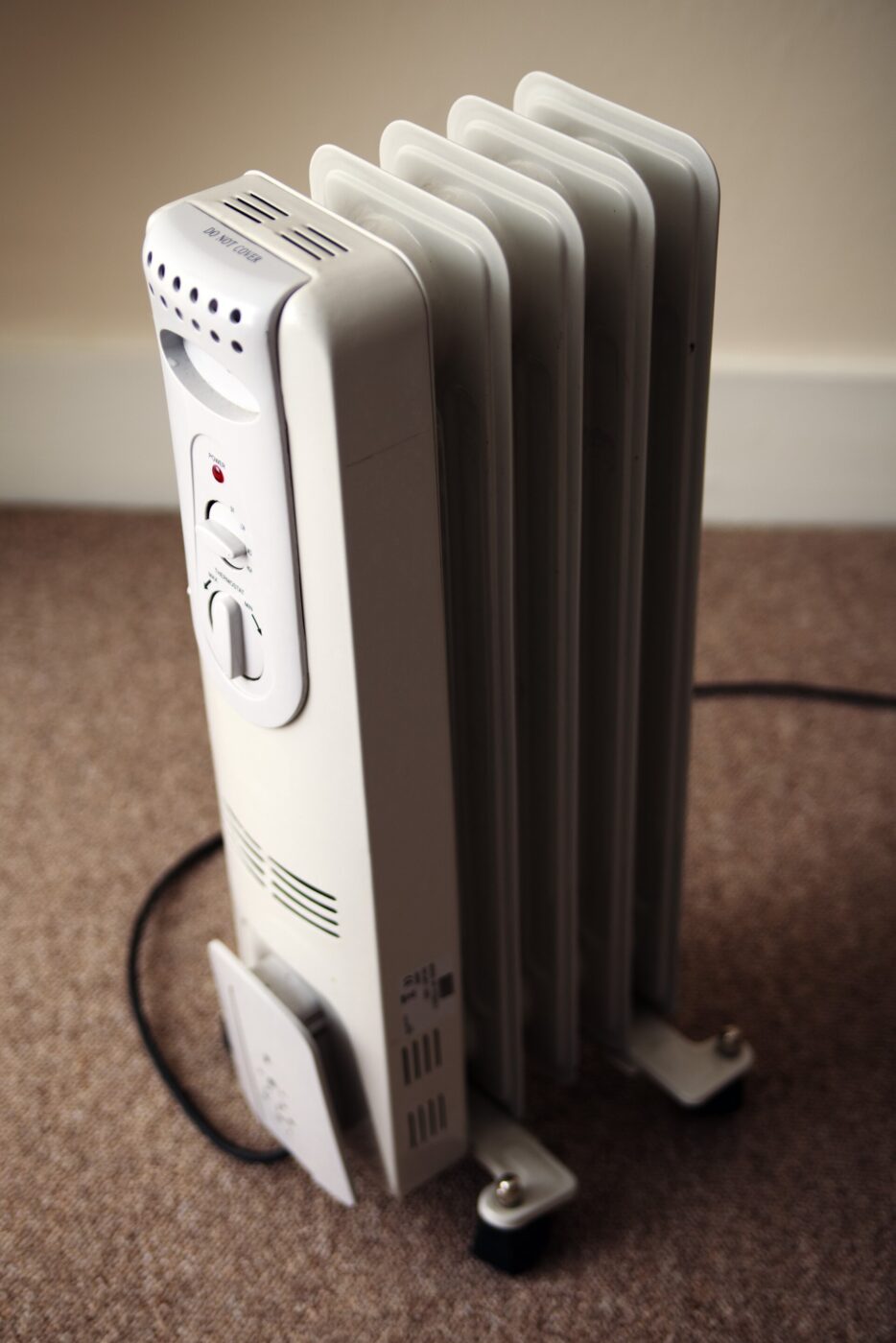 A tall white column-style oil-filled space heater plugged in by a wall.