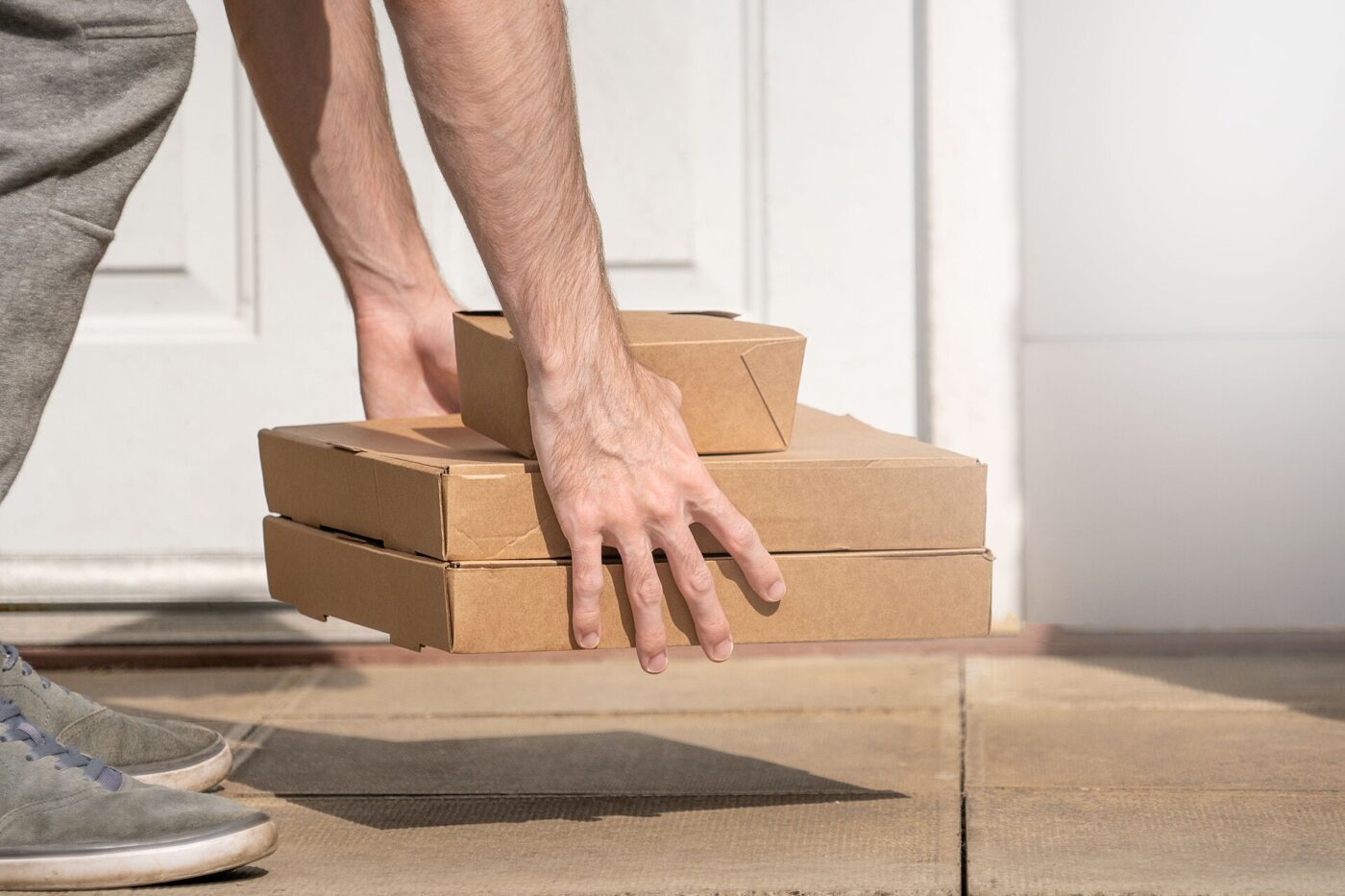 A delivery driver's arm placing stacked boxes at a front door.
