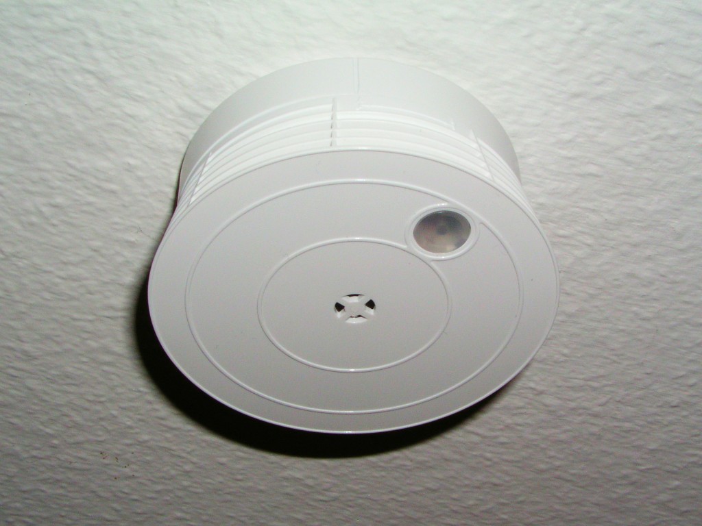 A round smoke detector mounted on a white ceiling.