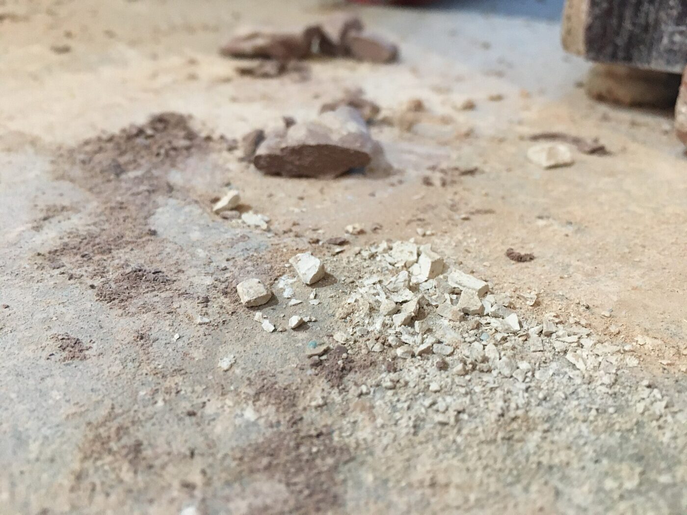 Close-up of dried clay fragments and pale dust scattered on a concrete studio floor.