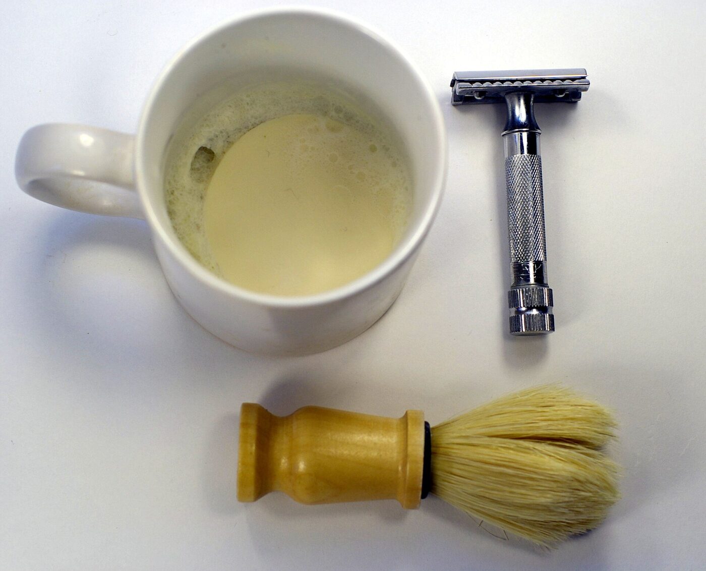 A safety razor shaving kit: razor, brush and a mug of lather.
