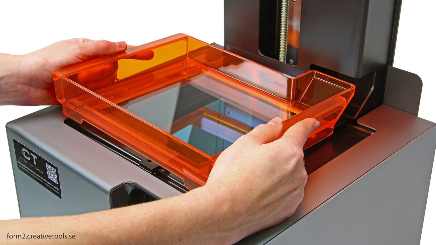 Opening the orange UV-blocking lid of a Formlabs Form 2 resin printer.