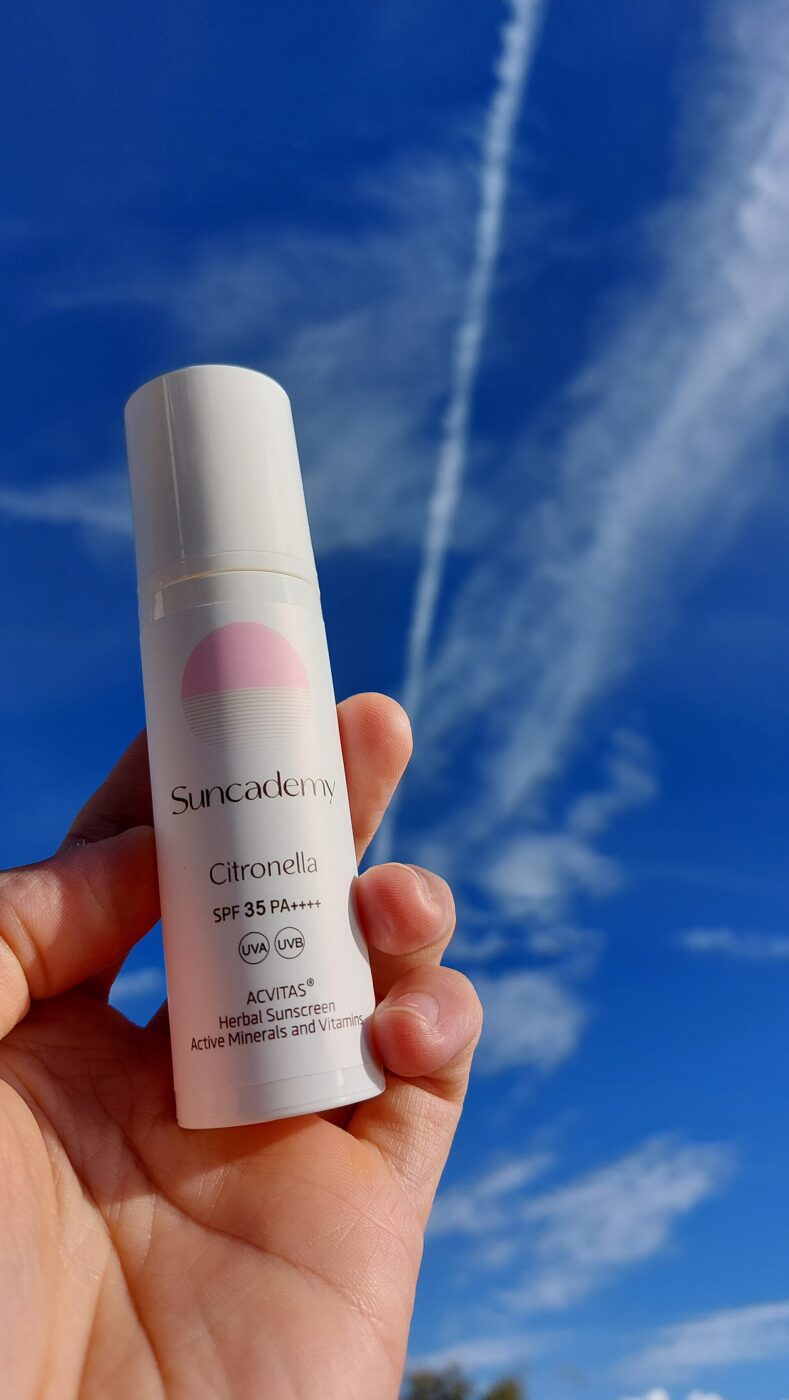 A hand holds a plain white sunscreen bottle outdoors.