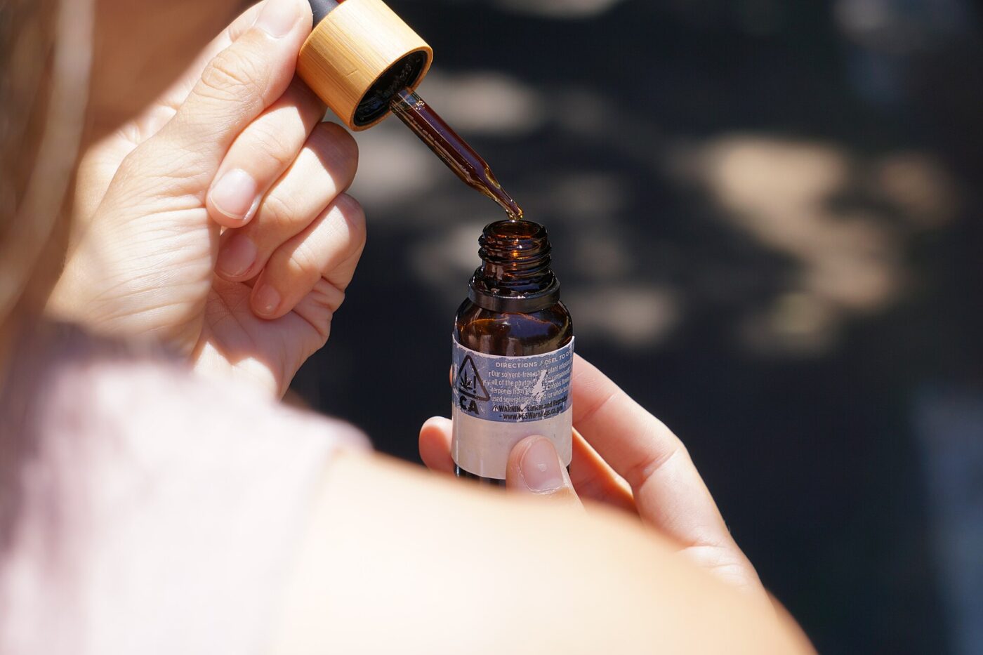A hand applies a serum from a dropper bottle onto a fingertip.