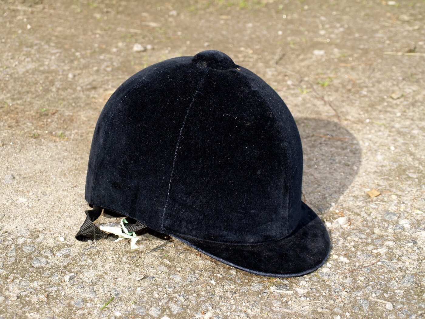 A black velvet riding helmet on sandy ground.