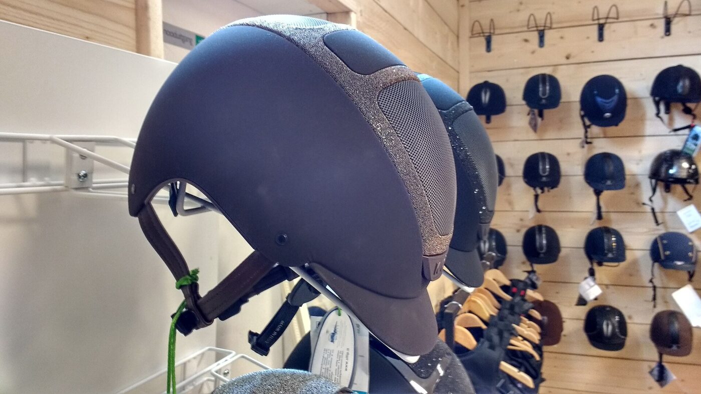 A navy riding helmet displayed in front of a wall of equestrian helmets.