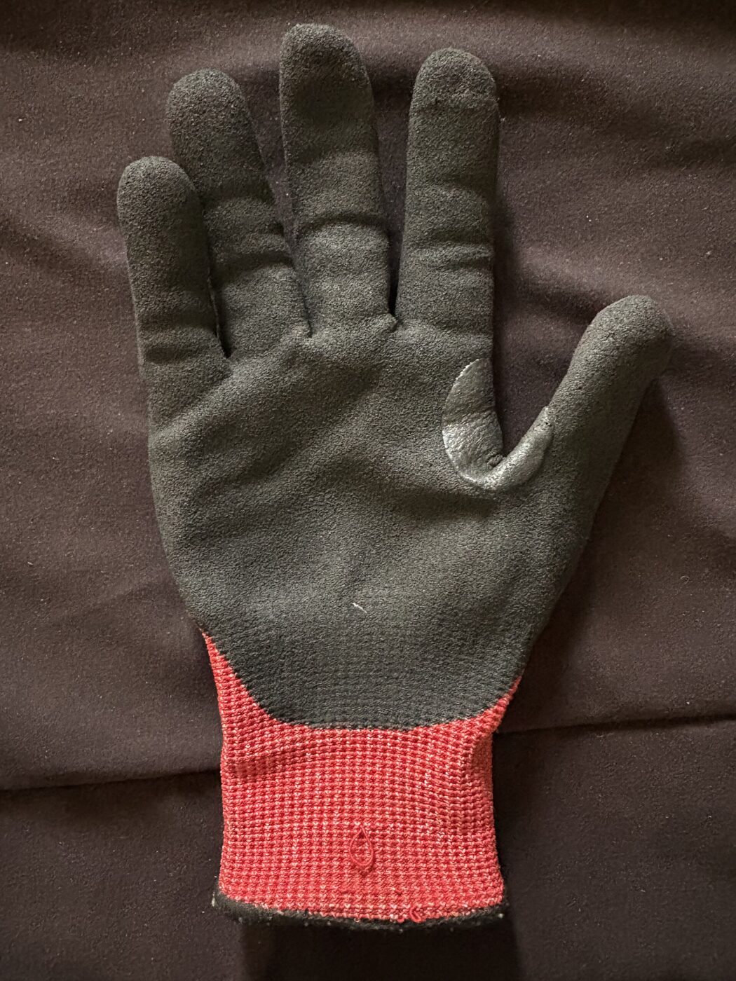 A black cut-resistant work glove with a red ribbed cuff laid palm-up on dark fabric.