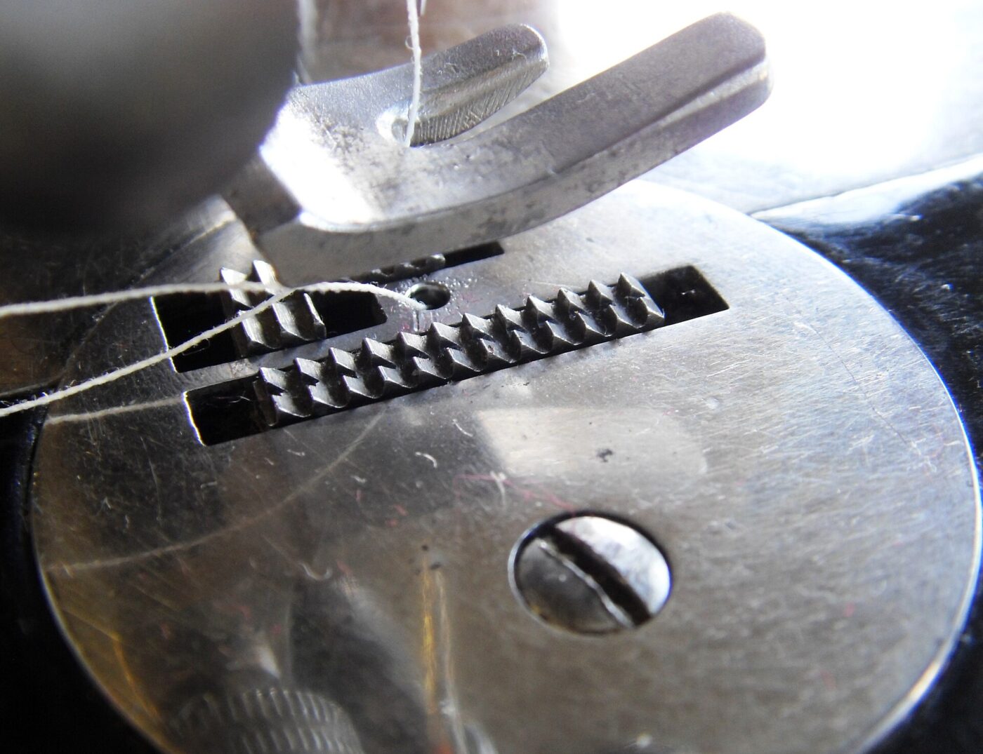 Metal feed dogs, needle plate and presser foot on a Singer domestic sewing machine, seen close up.