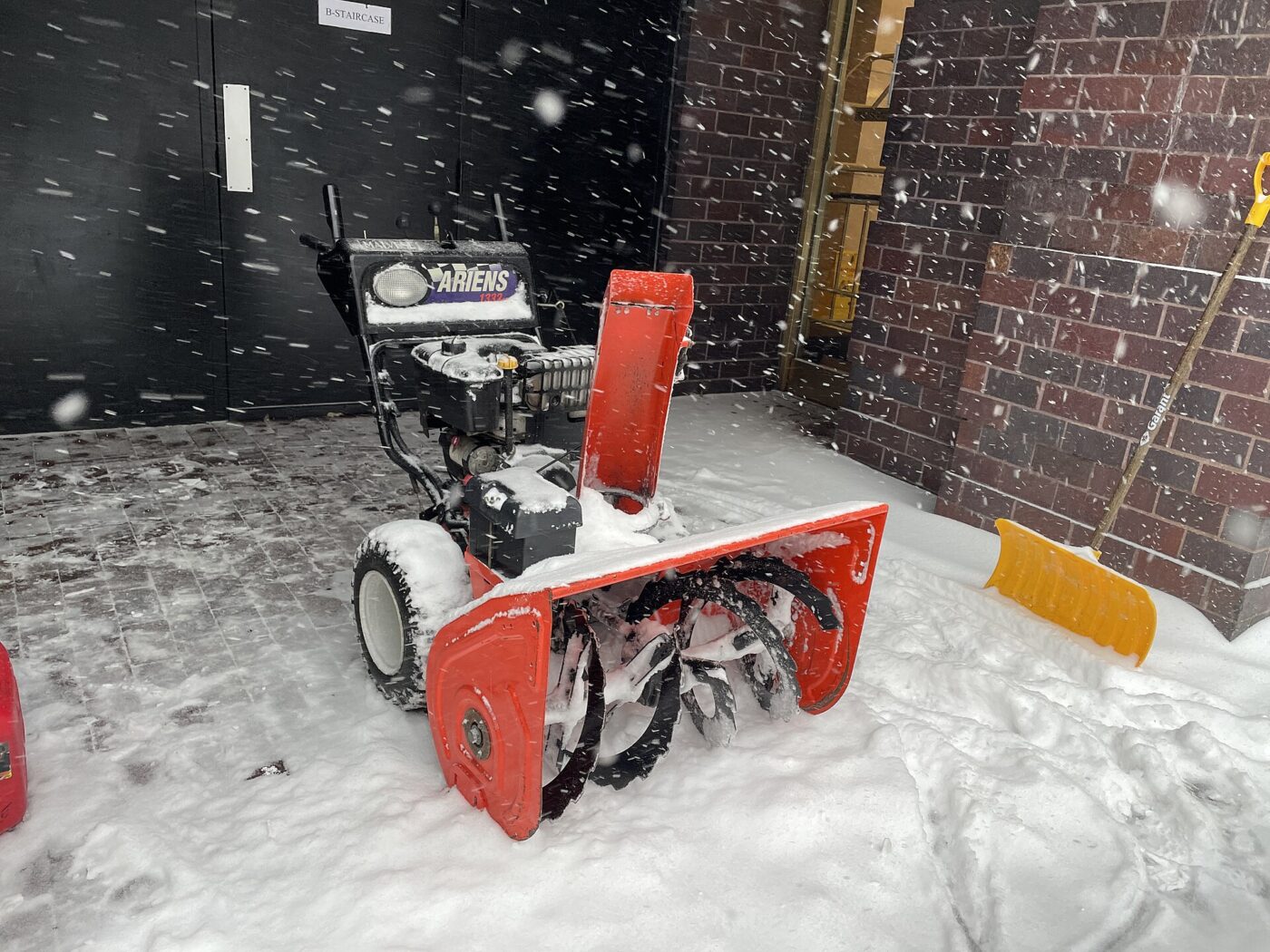 A red and black two-stage snow blower parked after a snowstorm.
