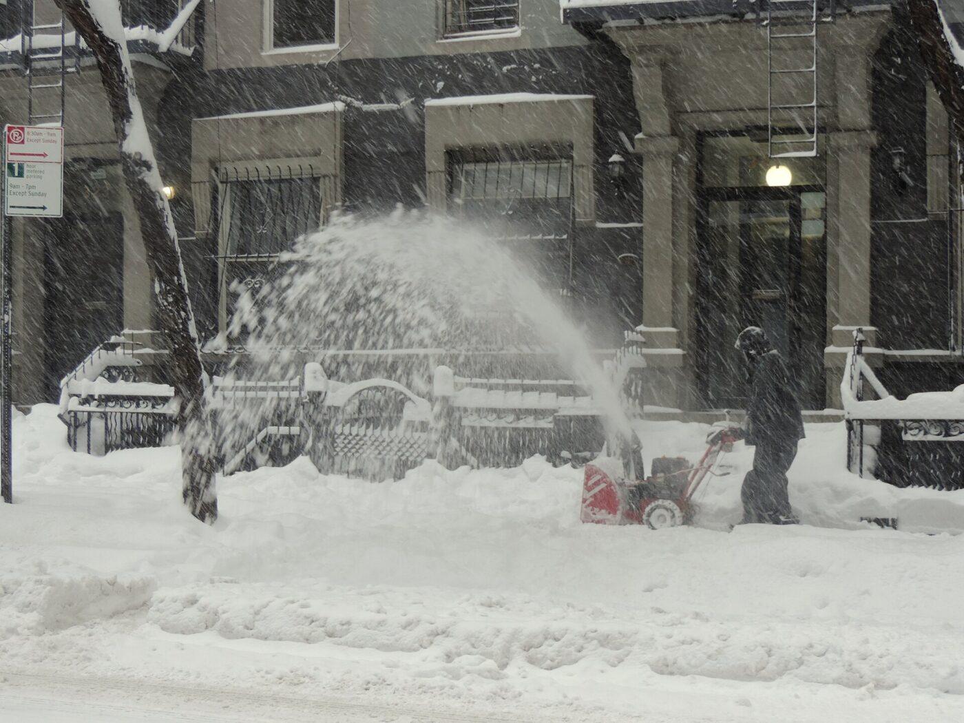 A person operating a snow blower on a snow-covered street.