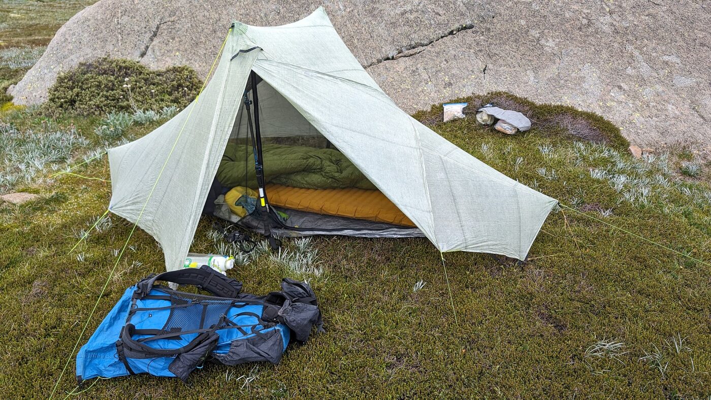 A tent, sleeping bag and backpack pitched on rocky ground.