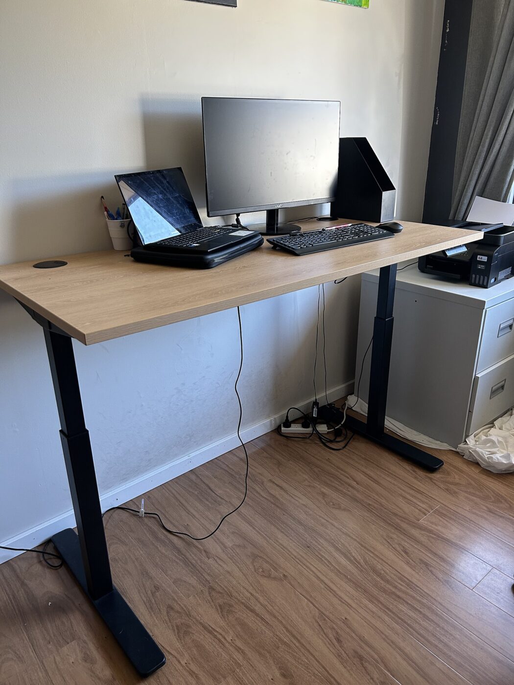 An electric height-adjustable desk raised up, with a monitor, laptop and keyboard on top.