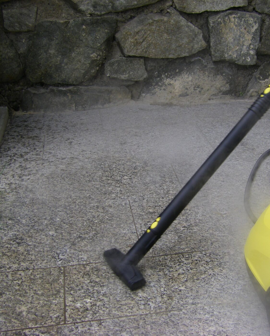A steam cleaner wand with a floor nozzle head being used on a floor.