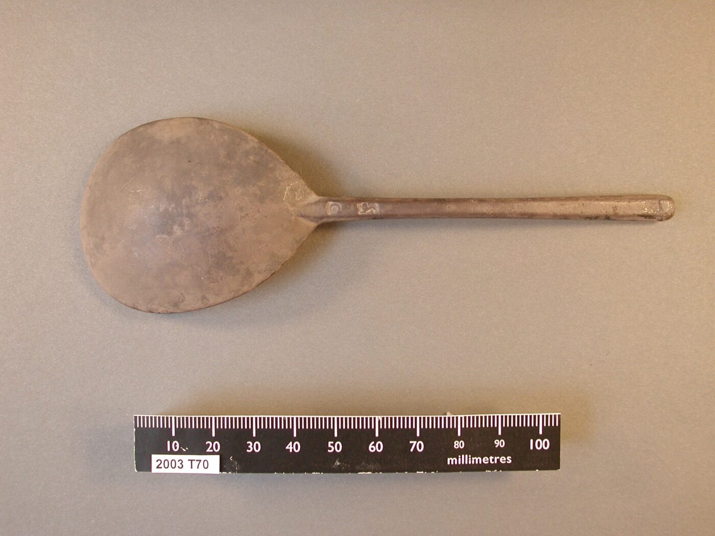 Blackened, tarnished silver spoon photographed with a small measuring scale.