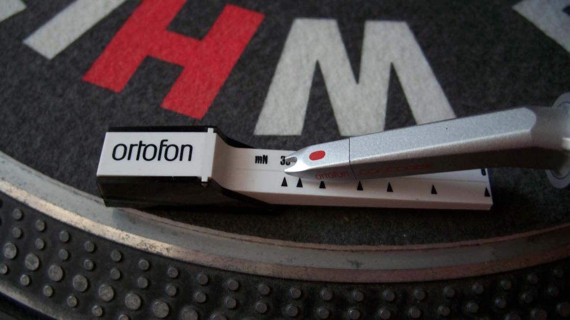 A stylus tracking-force gauge resting on a turntable platter beside the tonearm.