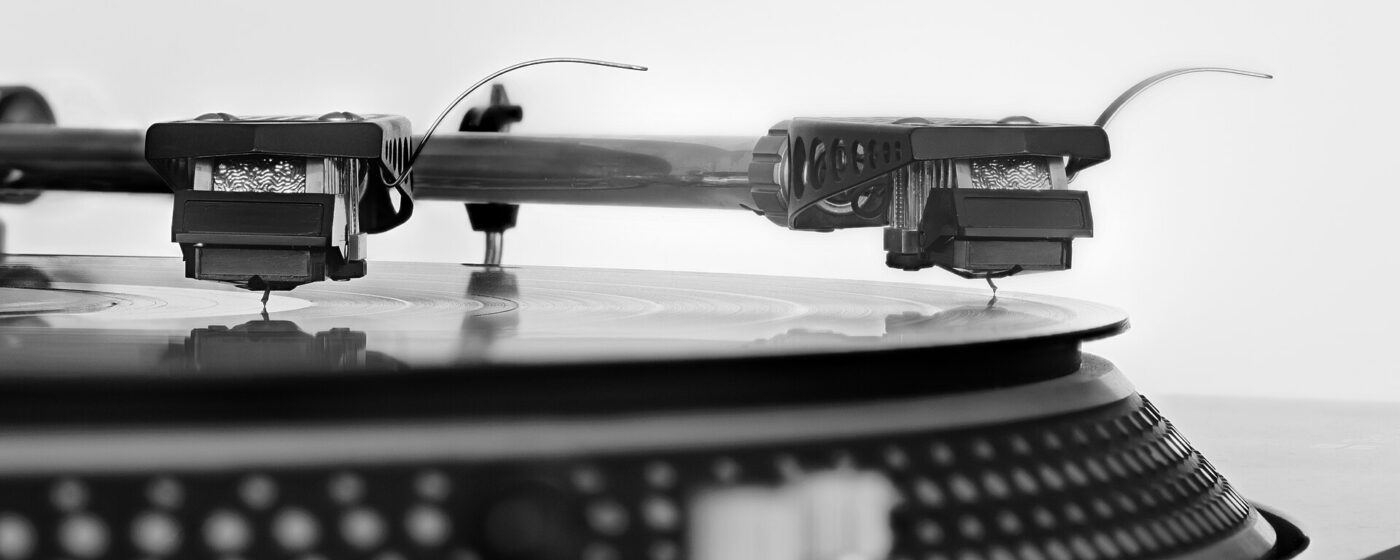 A record player's tonearm and needle tracking a groove across a vinyl record.