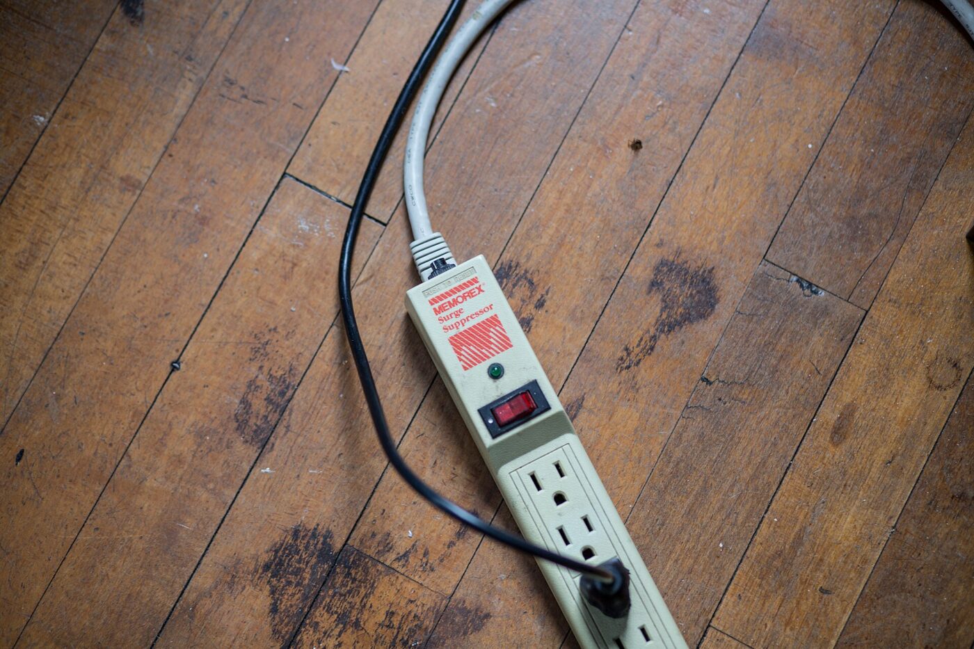 A plain power strip with a cord, plugged in on a wood floor.