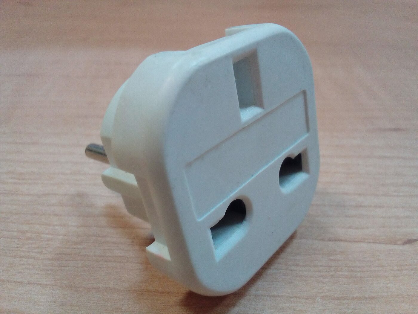 A UK-to-EU travel plug adapter photographed against a plain wood surface.