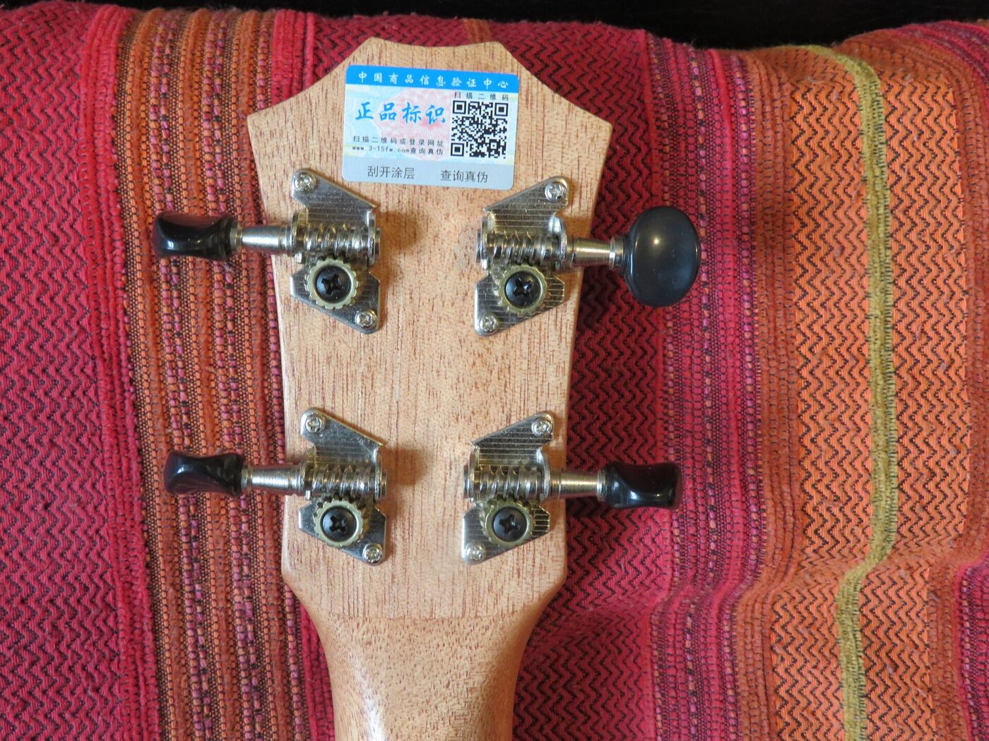 Close-up of a ukulele headstock with four open-gear tuning pegs and strings.
