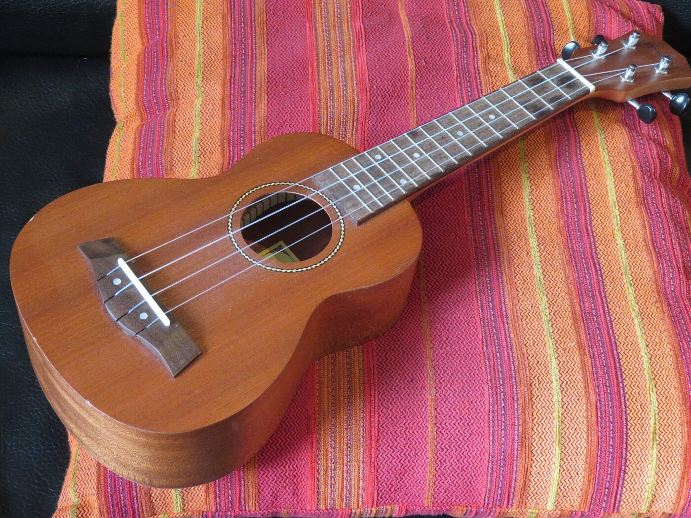 A soprano ukulele with a mahogany body resting on a striped cushion.