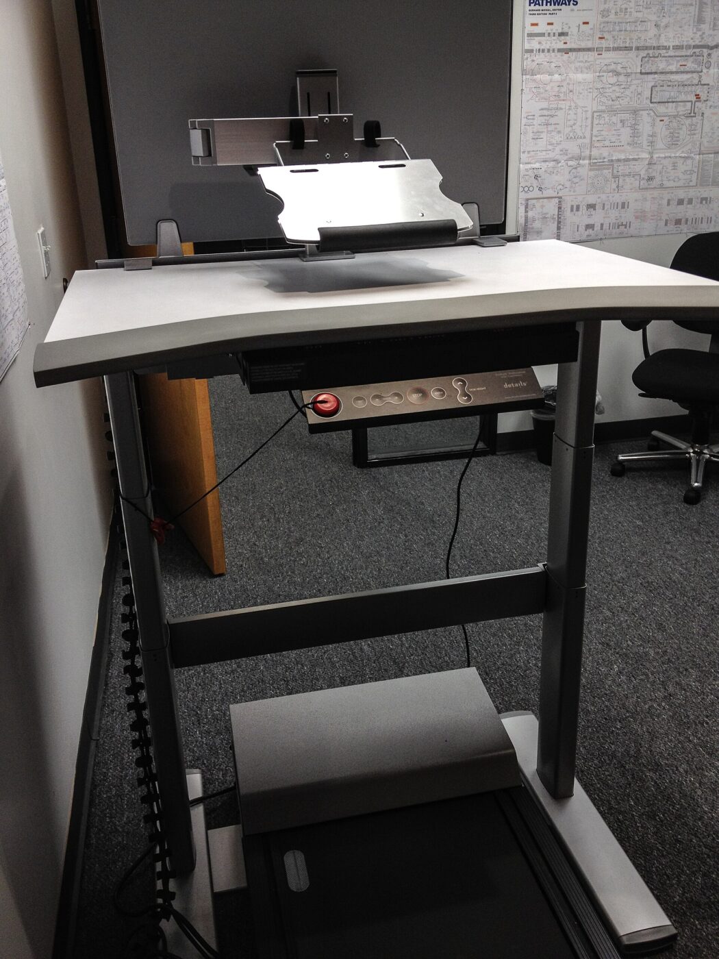 Slim treadmill base positioned under a height-adjustable desk platform, no one using it.