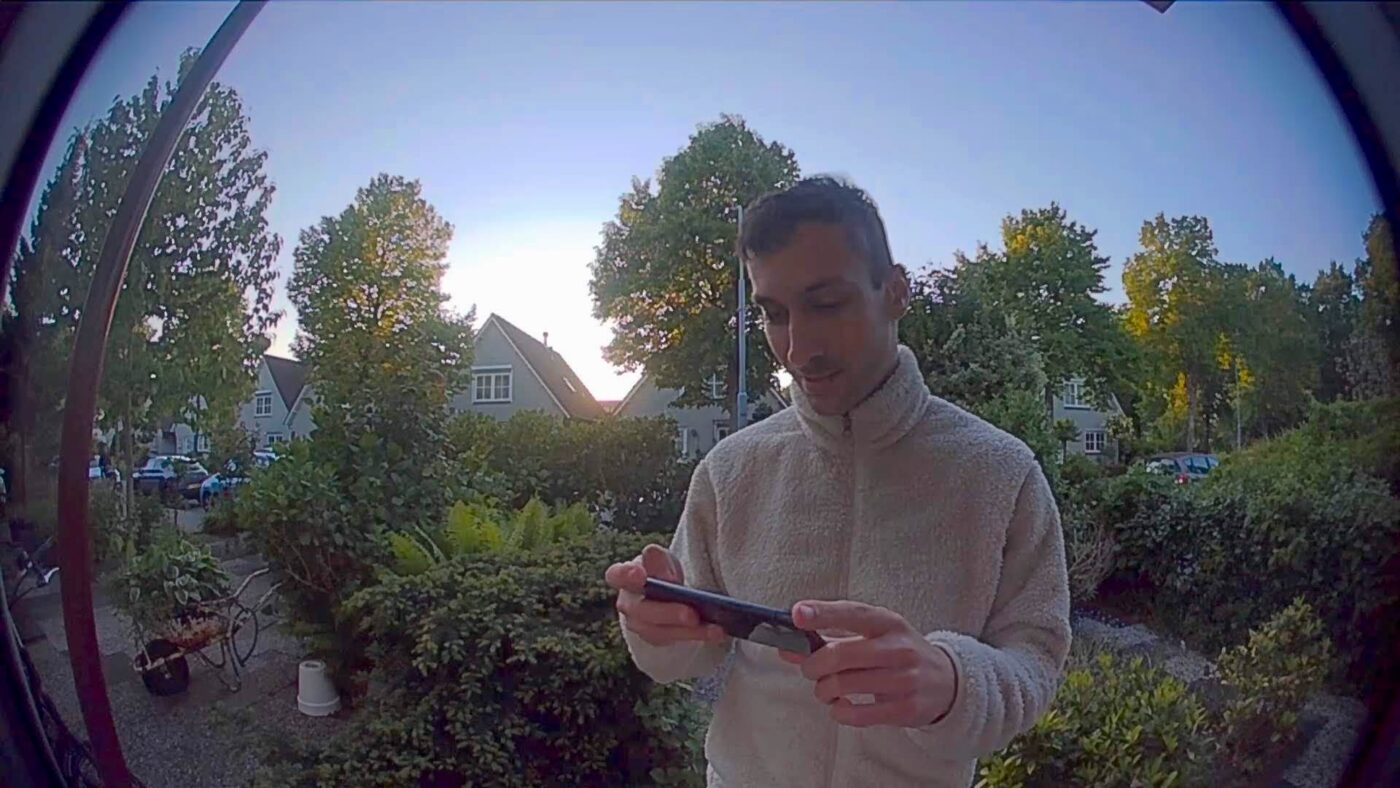 Fisheye video doorbell footage showing a person standing at the door looking at a phone.