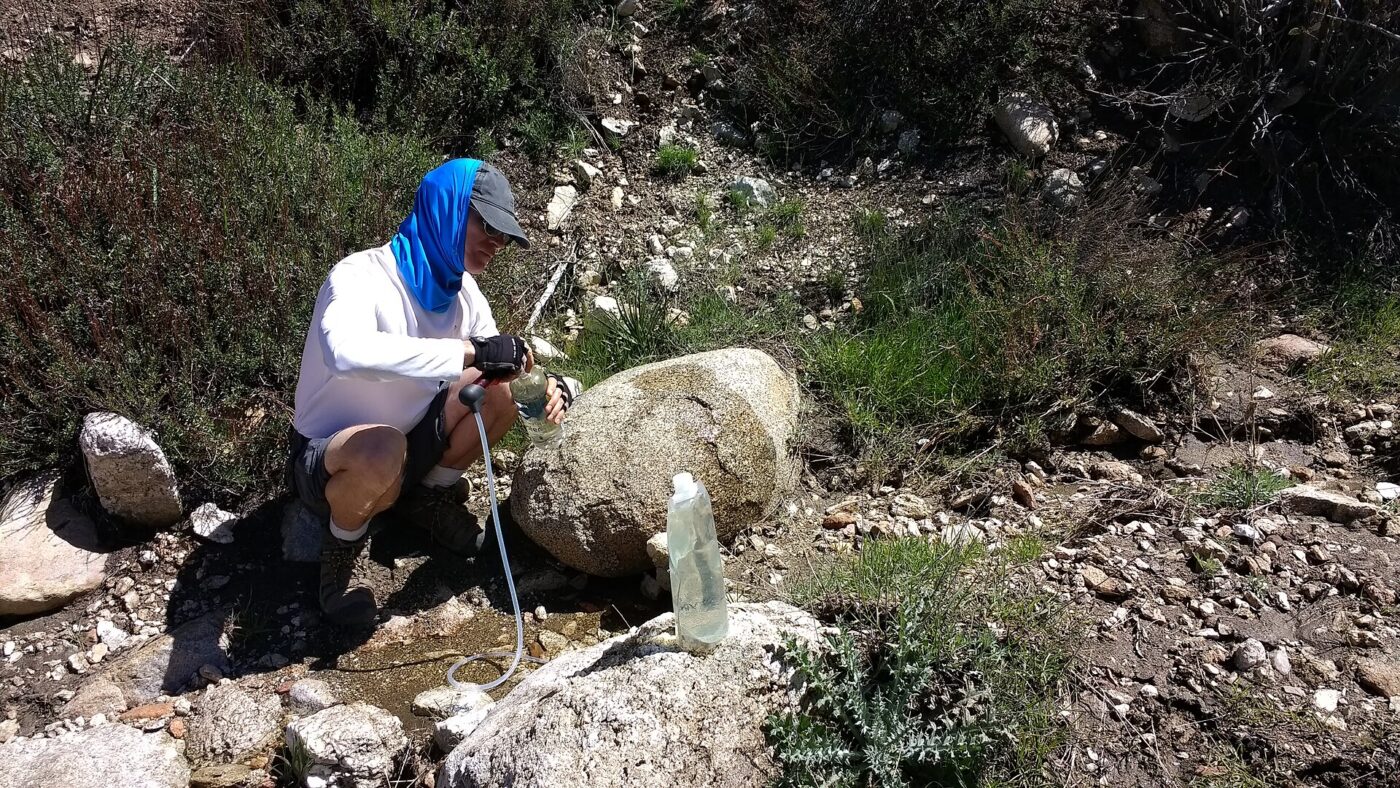 A hiker filtering water from an intermittent stream on a backcountry trail.