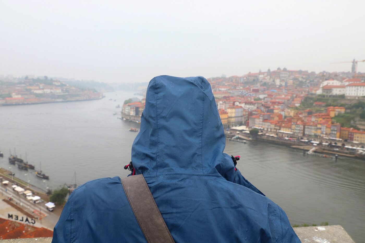 A person wearing a hooded waterproof outdoor jacket in the rain, seen from behind.