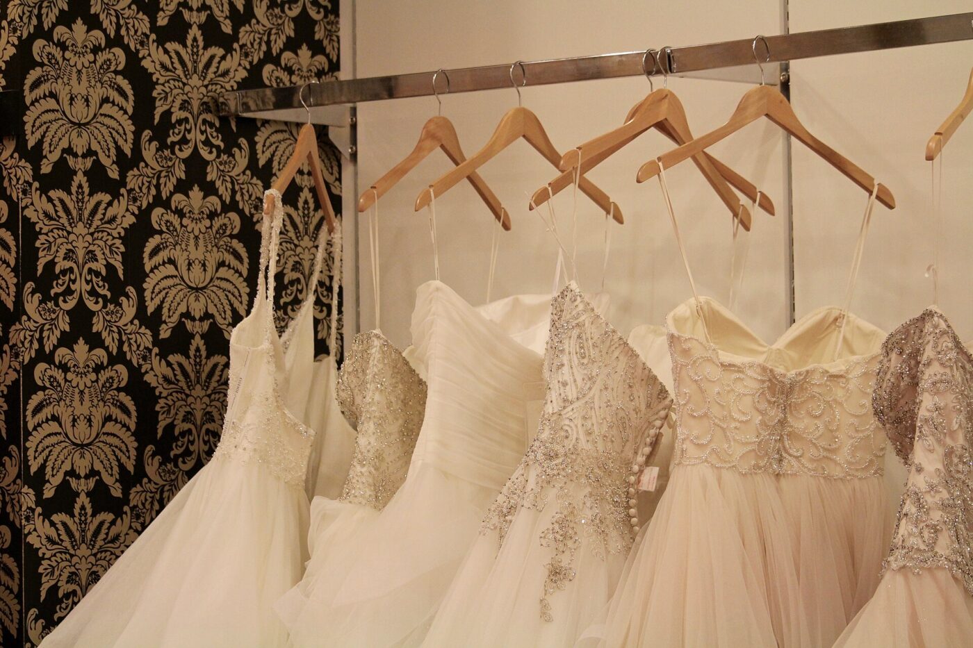 Row of wedding dresses in varying styles hanging on wooden hangers.