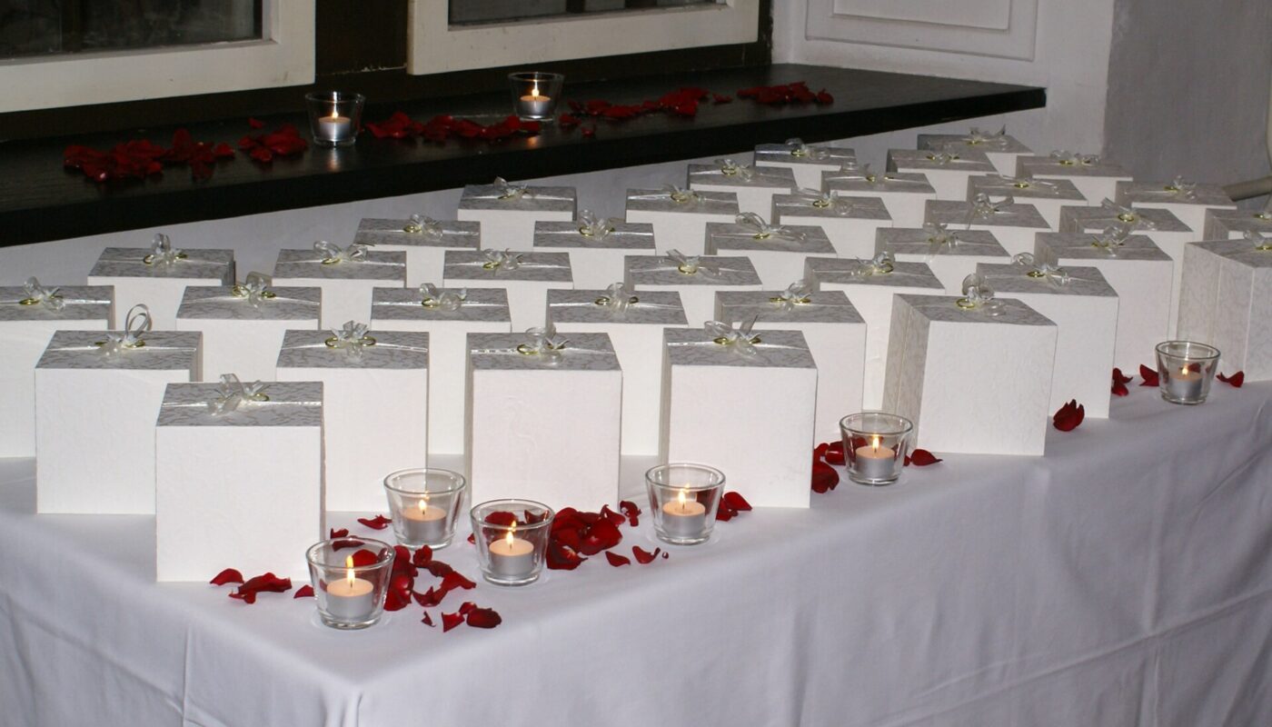 Boxed wedding favors set out on a table with tea lights and rose petals.