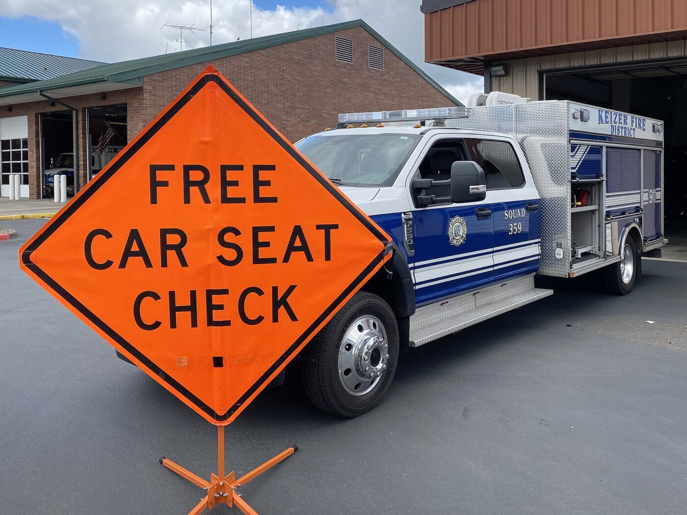 Orange road sign reading Free Car Seat Check, positioned in front of a fire department truck.
