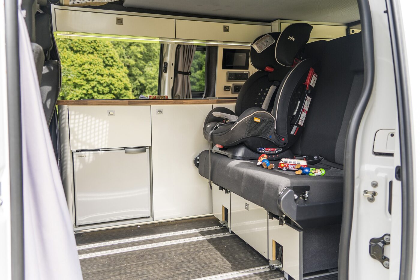 Child car seat with five-point harness straps installed in the back of a camper van, no child seated.