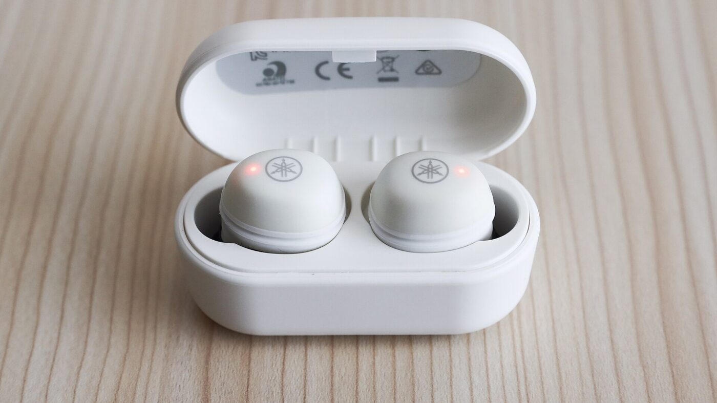 A pair of white true wireless earbuds sitting in an open charging case on a wooden surface