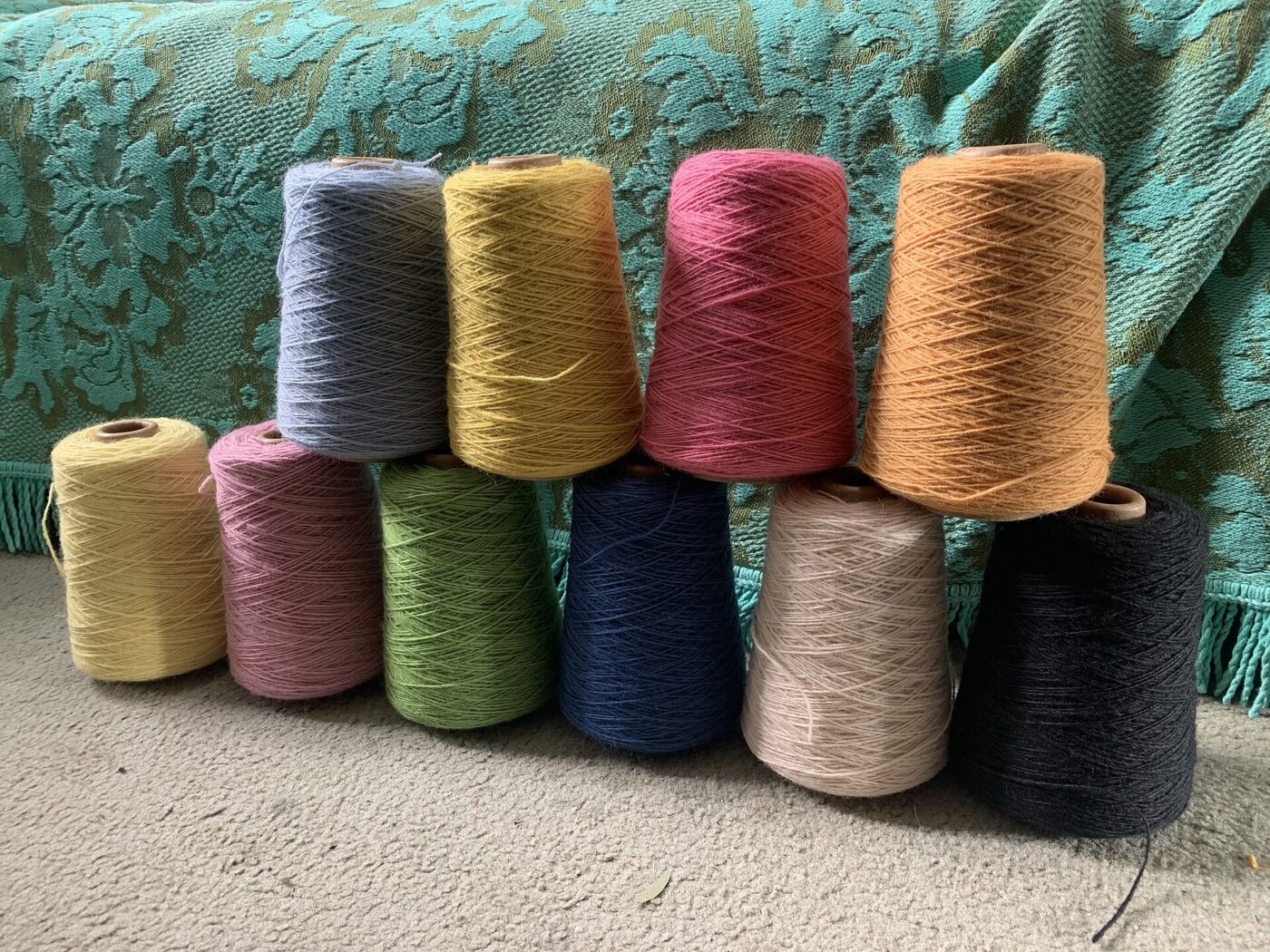 Multiple cones of yarn in different colors and thread thicknesses resting on folded fabric.
