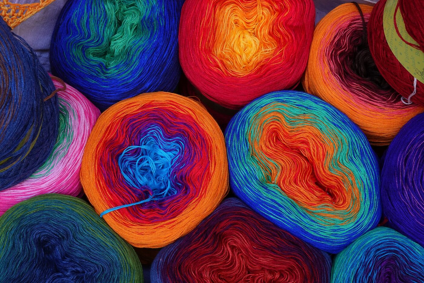 Dozens of rainbow-colored yarn balls and skeins stacked together in a shop display.